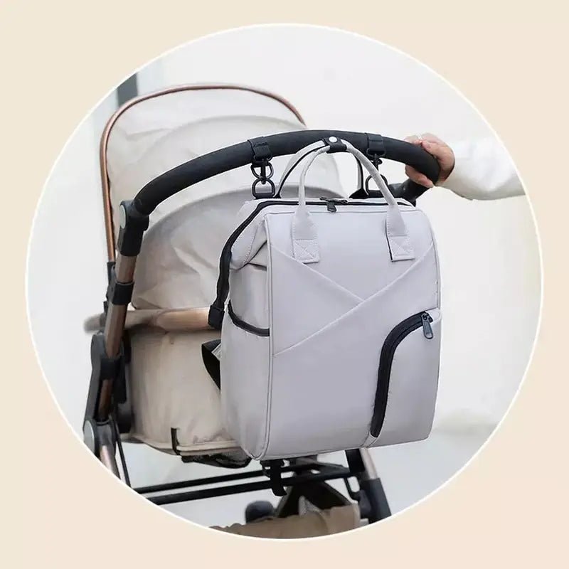 Sac à dos à langer chic gris clair avec plusieurs poches suspendu sur une poignée de poussette