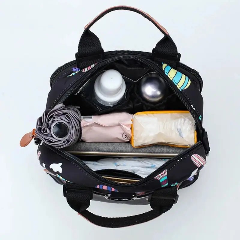 Sac à dos à langer noir avec motifs de montgolfières, contenant bouteilles et parapluie